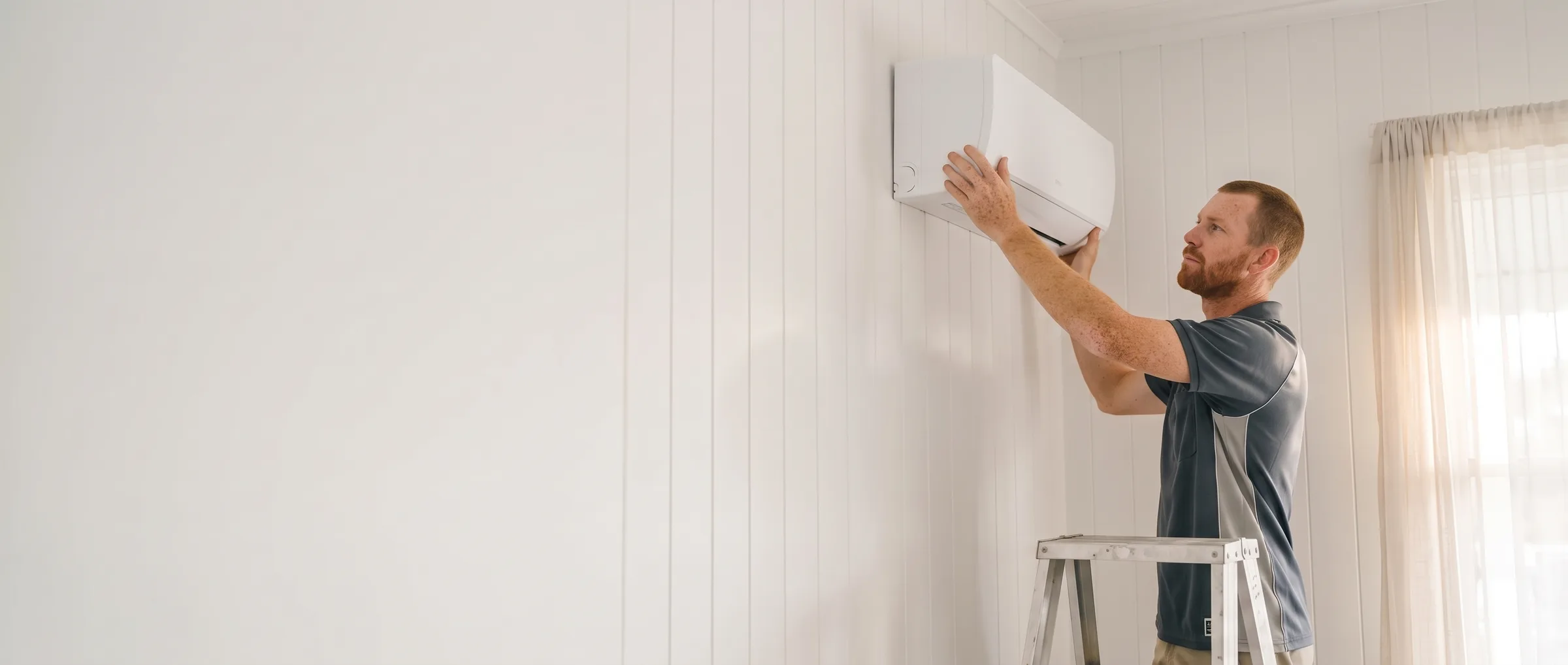 ABS electrician seating a split system indoor unit onto its bracket in a Queenslander bedroom