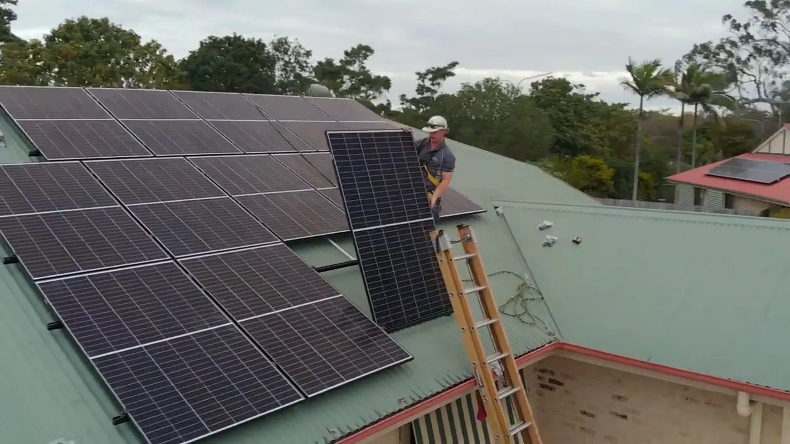 Drone view of an ABS electrician lifting a solar panel onto a Brisbane roof